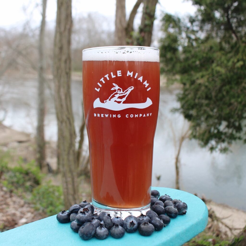 Little Miami Brewing Company's rooftop patio with string lights, outdoor seating, and people under a blue summer sky.