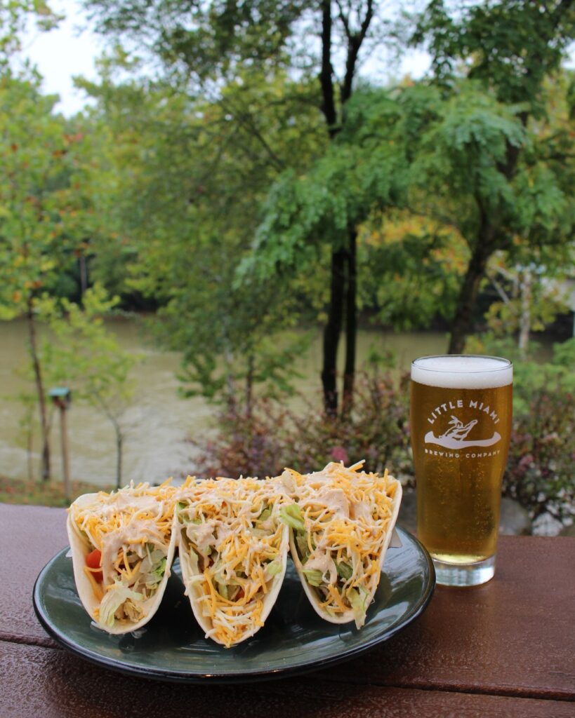Little Miami Brewing Company’s beer and tacos in front of the Little Miami River in Ohio, offering a picturesque dining experience by the water.