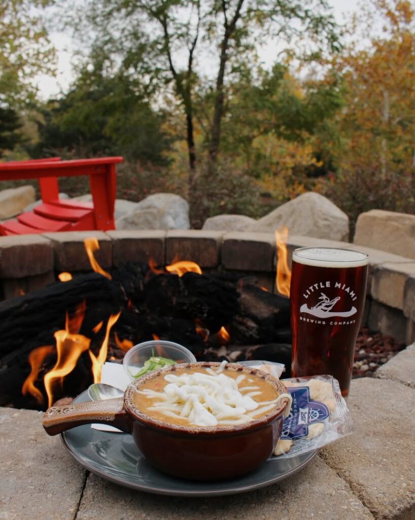 A bowl of White Chicken Chili topped with cheese and sour cream, served with a jalapeño slice at Little Miami Brewing Company.