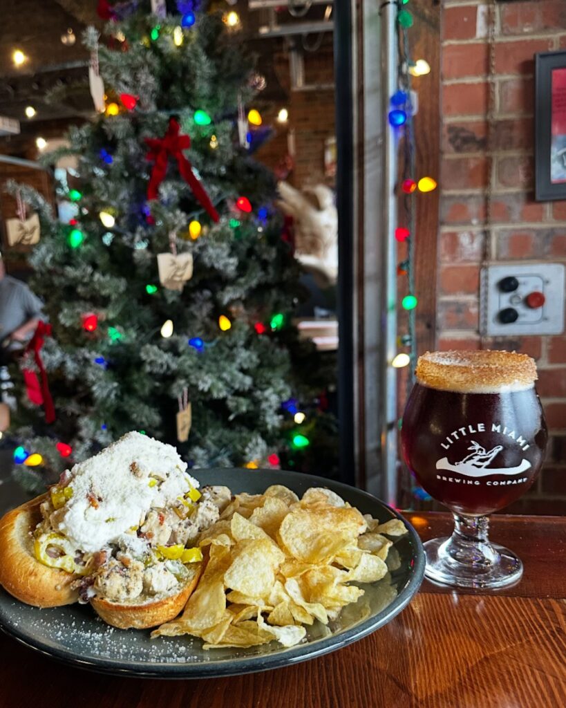 Classic Chicken Rancher sandwich with chips and a pint of beer at Little Miami Brewing Company, set in front of a decorated Christmas tree.