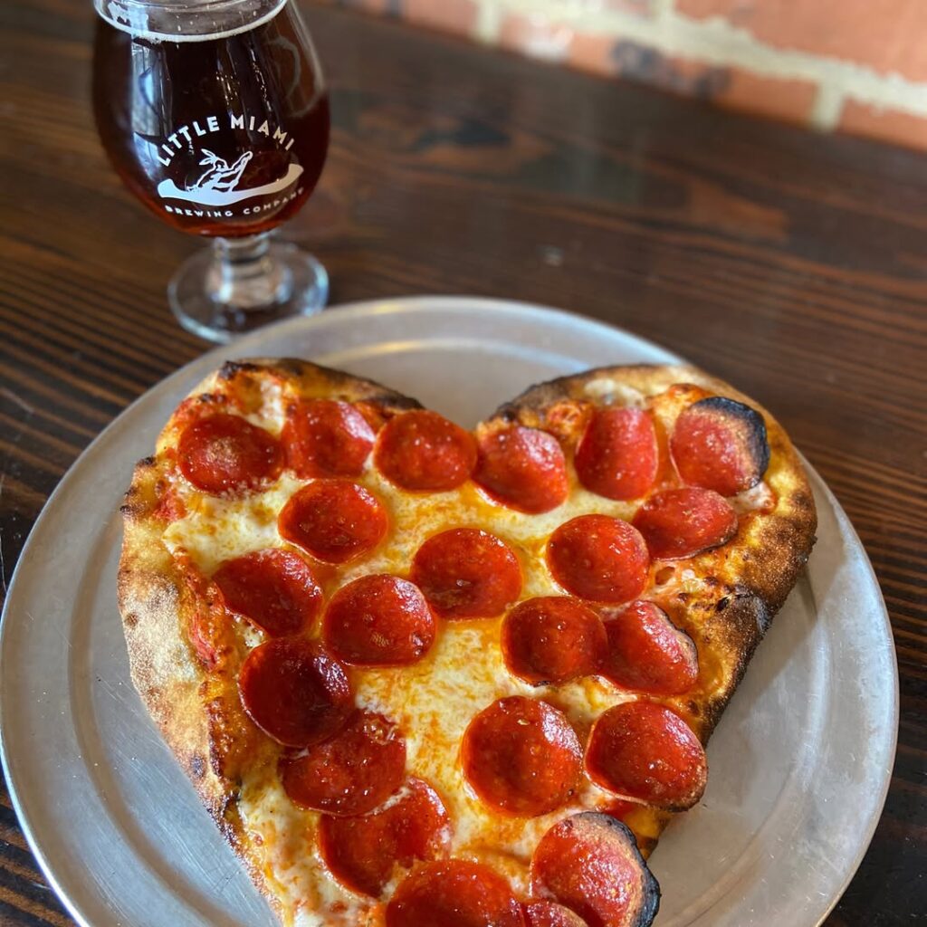 A glass of beer and a heart-shaped pepperoni pizza on a table at Little Miami Brewing Company during Valentine’s Day.