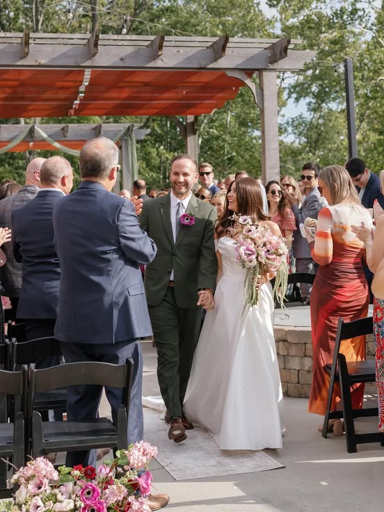 Bride and groom celebrating under a floral pergola at an outdoor wedding ceremony.
