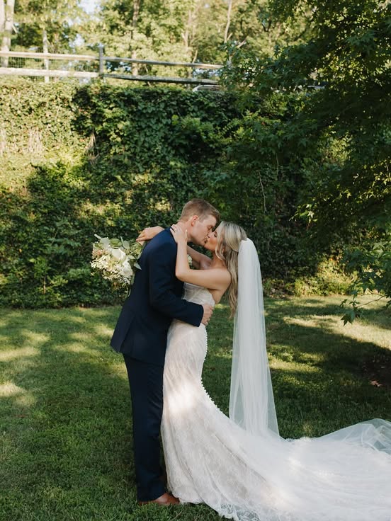 Bride and groom sharing a kiss outdoors in front of a rustic venue on a sunny day.