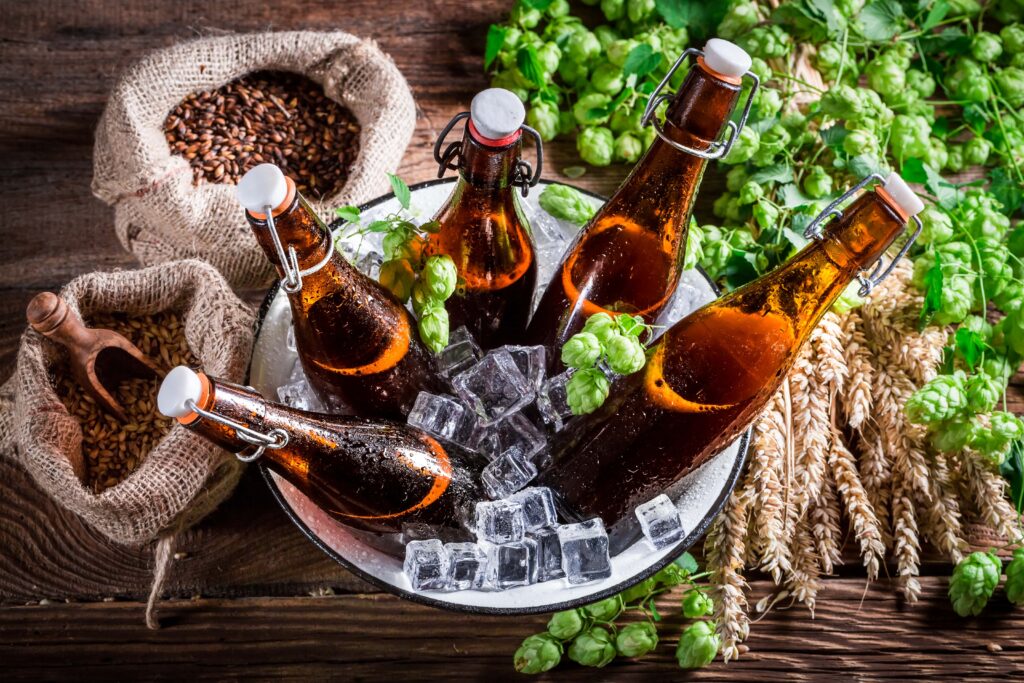 A bowl of ice-cold beer bottles sits on a wooden table surrounded by hops, barley, and wheat. This could be a scene from Little Miami Brewing in Cincinnati.