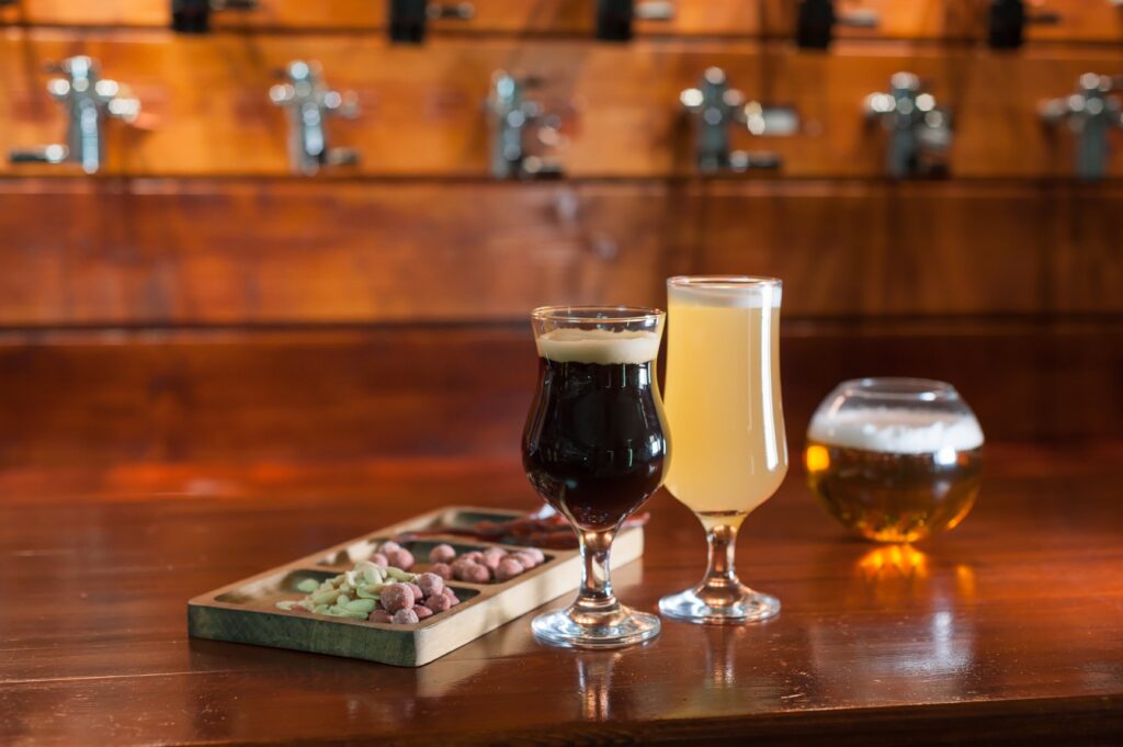 Three beers and snacks on a bar counter with beer taps in the background. This could be a scene from breweries in Cincinnati . 