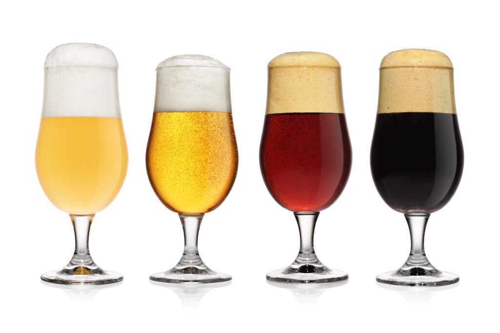 Four glasses of beer with varying alcohol content are lined up on a white background. From left to right, the beers range from pale yellow to dark brown, with increasing foam head.