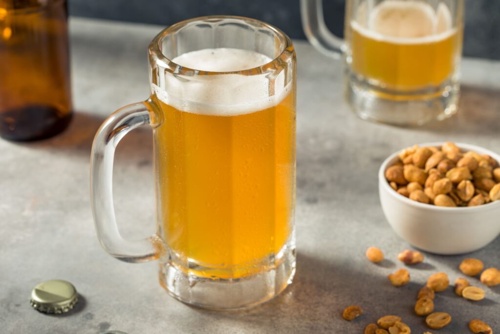 A  mug of golden pilsner beer sits on a table with a bowl of peanuts.