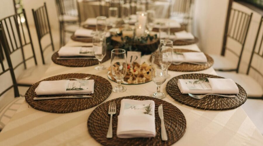 Elegant rehearsal dinner table setup with woven placemats, neatly folded napkins, and a rustic floral centerpiece.