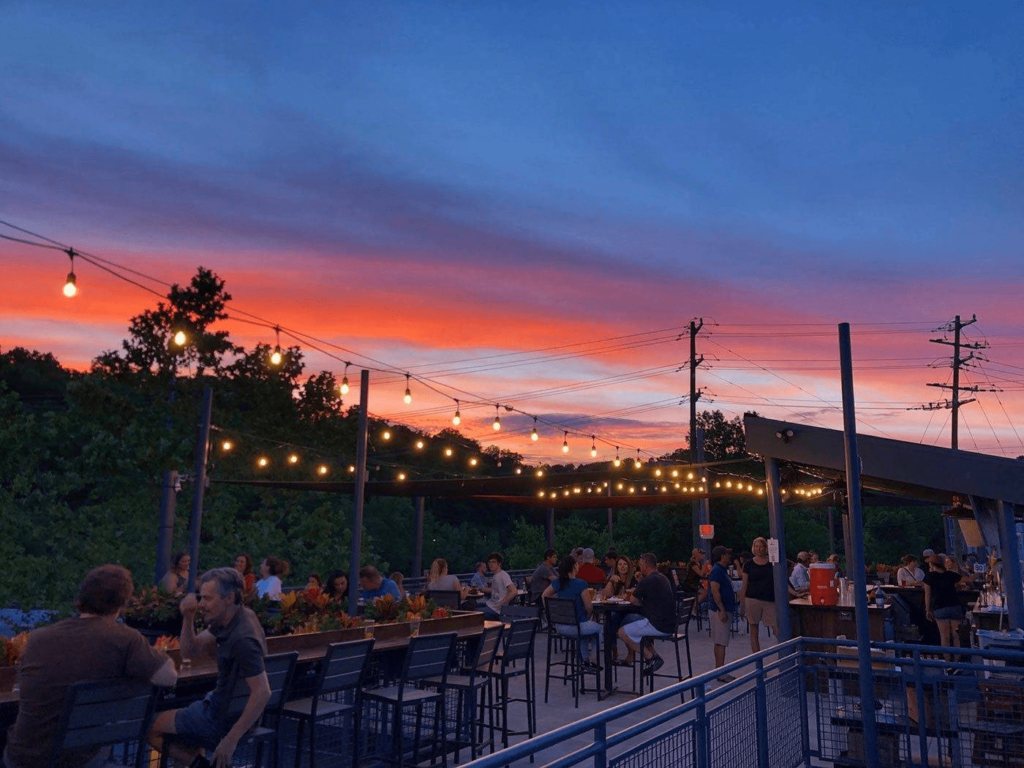 A vibrant outdoor brewery setting at sunset, with people enjoying drinks under string lights, ideal for brewery trips near me.