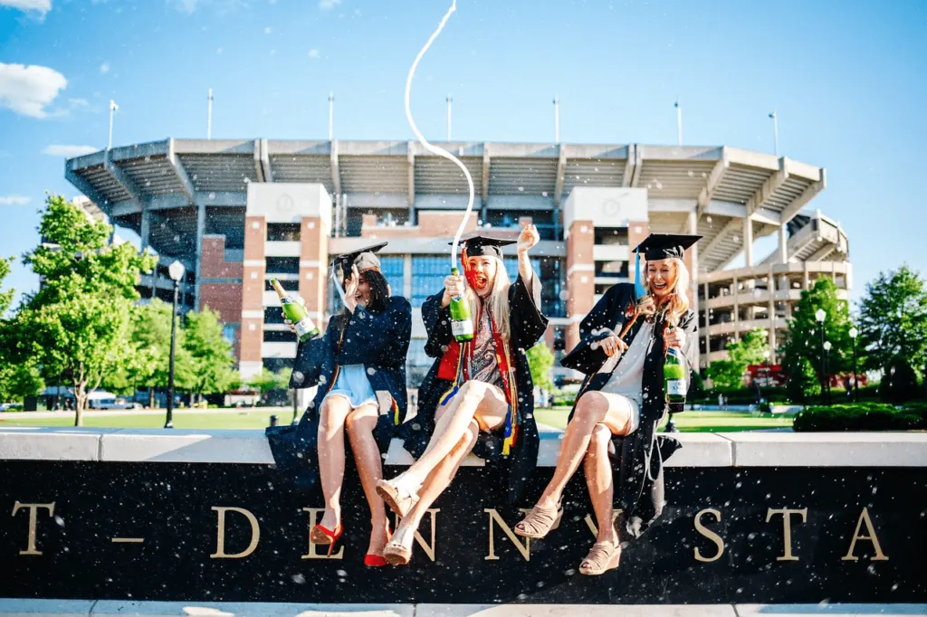 three excited graduates sitting on a low wall