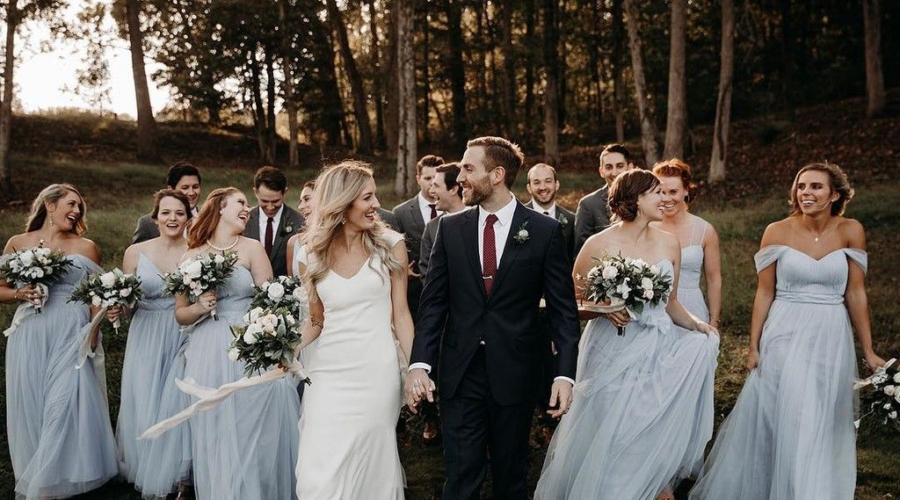 A bride and groom walk joyfully with their wedding party in an outdoor setting.