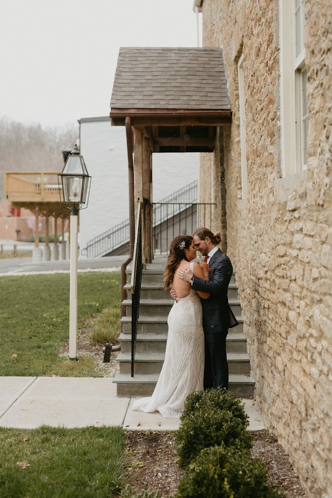 A bride and groom share an intimate moment near a rustic stone building.