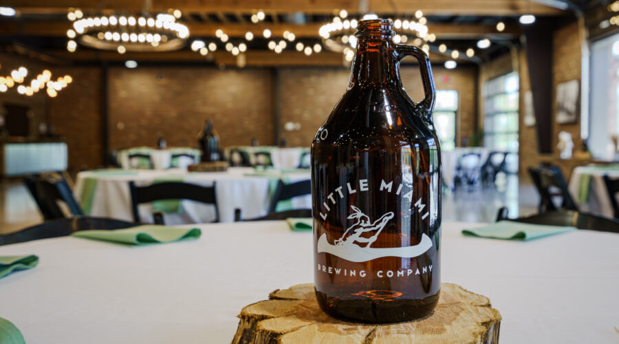 A brown glass growler from Little Miami Brewing Company on a wooden coaster on a white table.