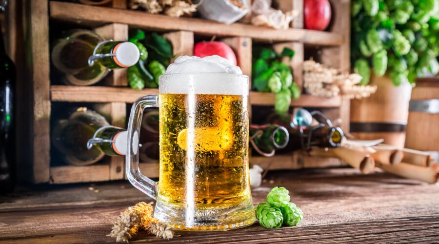 A frosty beer mug with fresh hops and wheat, capturing the essence of breweries in Cincinnati. Rustic shelves of bottles and ingredients in the background.