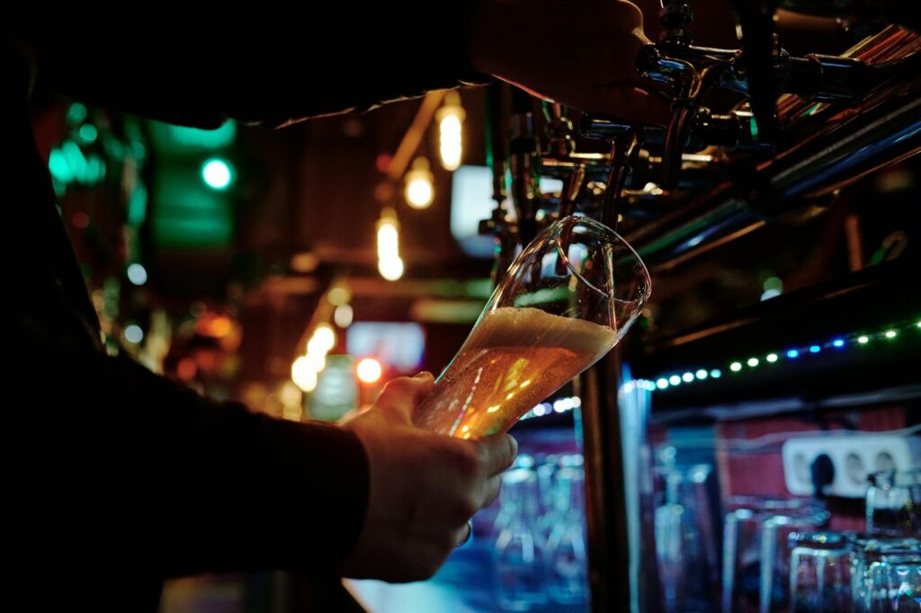 A bartender pours a golden beer from a tap in a dimly lit bar, showcasing Cincinnati's brewing history 