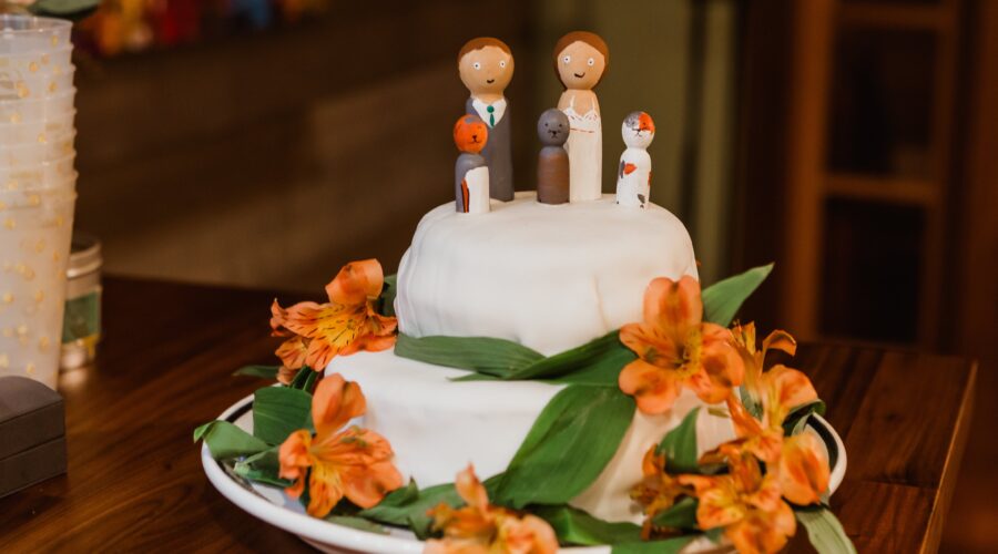 A two-tier wedding cake adorned with orange flowers and green leaves, set on a wooden table, ideal for outdoor wedding venues.