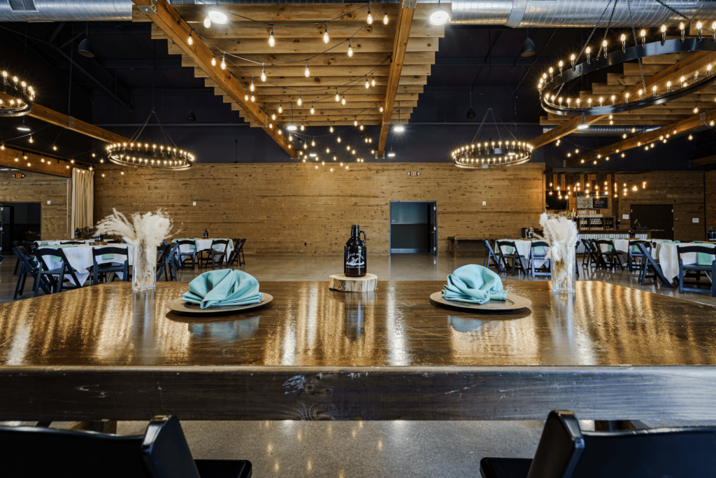 Rustic event venue, perfect for a rehearsal dinner. Wooden ceiling with hanging lights, tables set for guests.