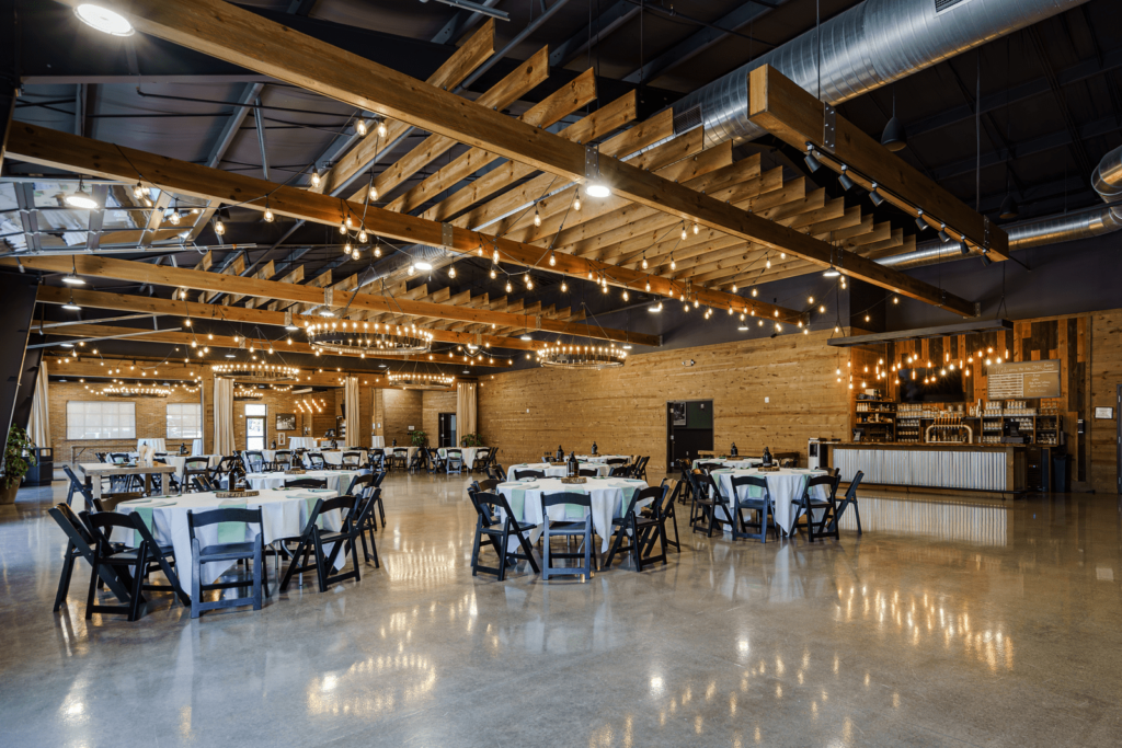 Rustic venue for a rehearsal dinner, with string lights, round tables, and a cozy bar, creating a warm and inviting ambiance.