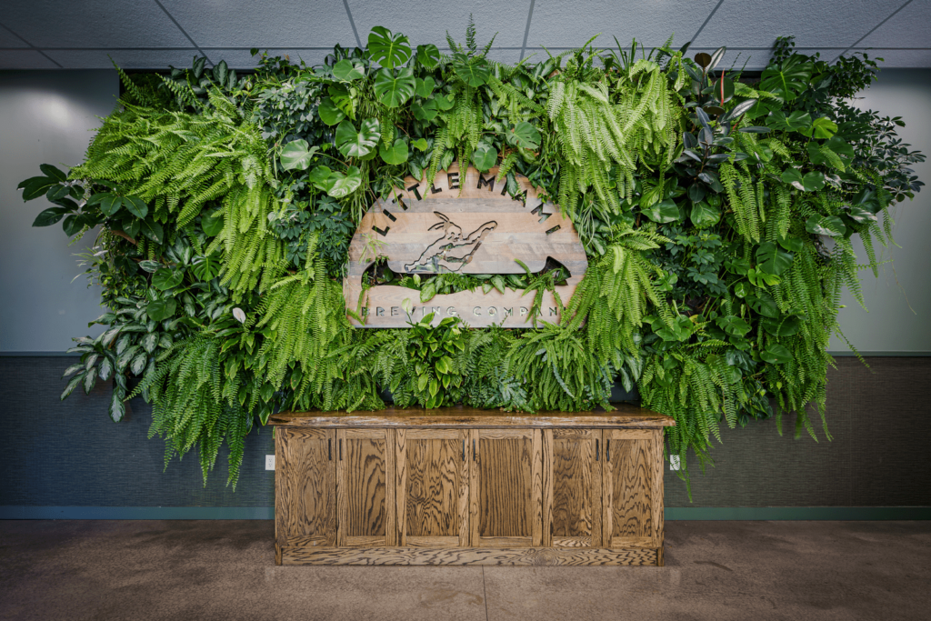 Green wall backdrop with lush foliage and a rustic wooden logo, creating a fresh and natural vibe for the space