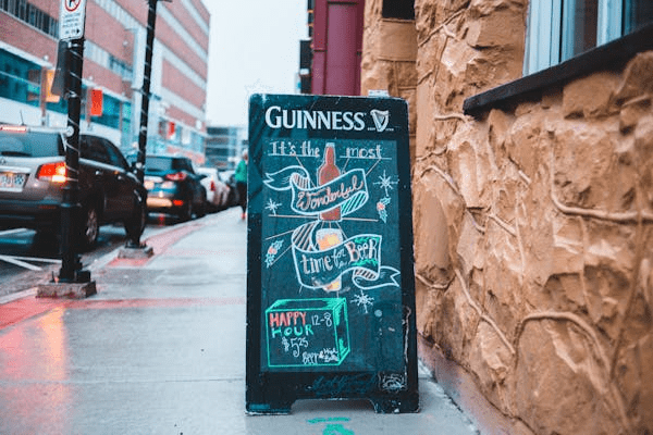 A chalkboard sign advertising Guinness beer with seasonal brews and a special happy hour price.