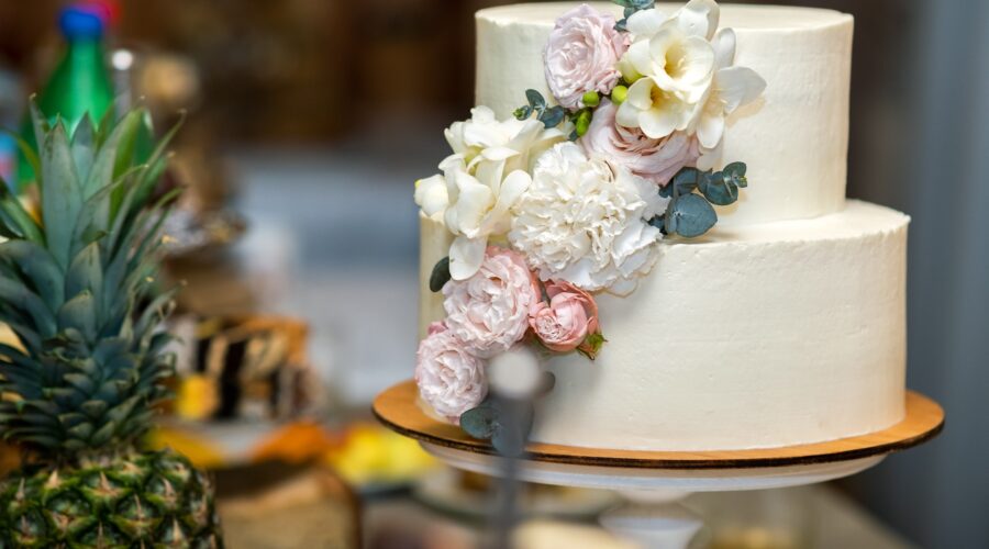 A two-tiered wedding cake adorned with fresh pink and white flowers cascading down the side.