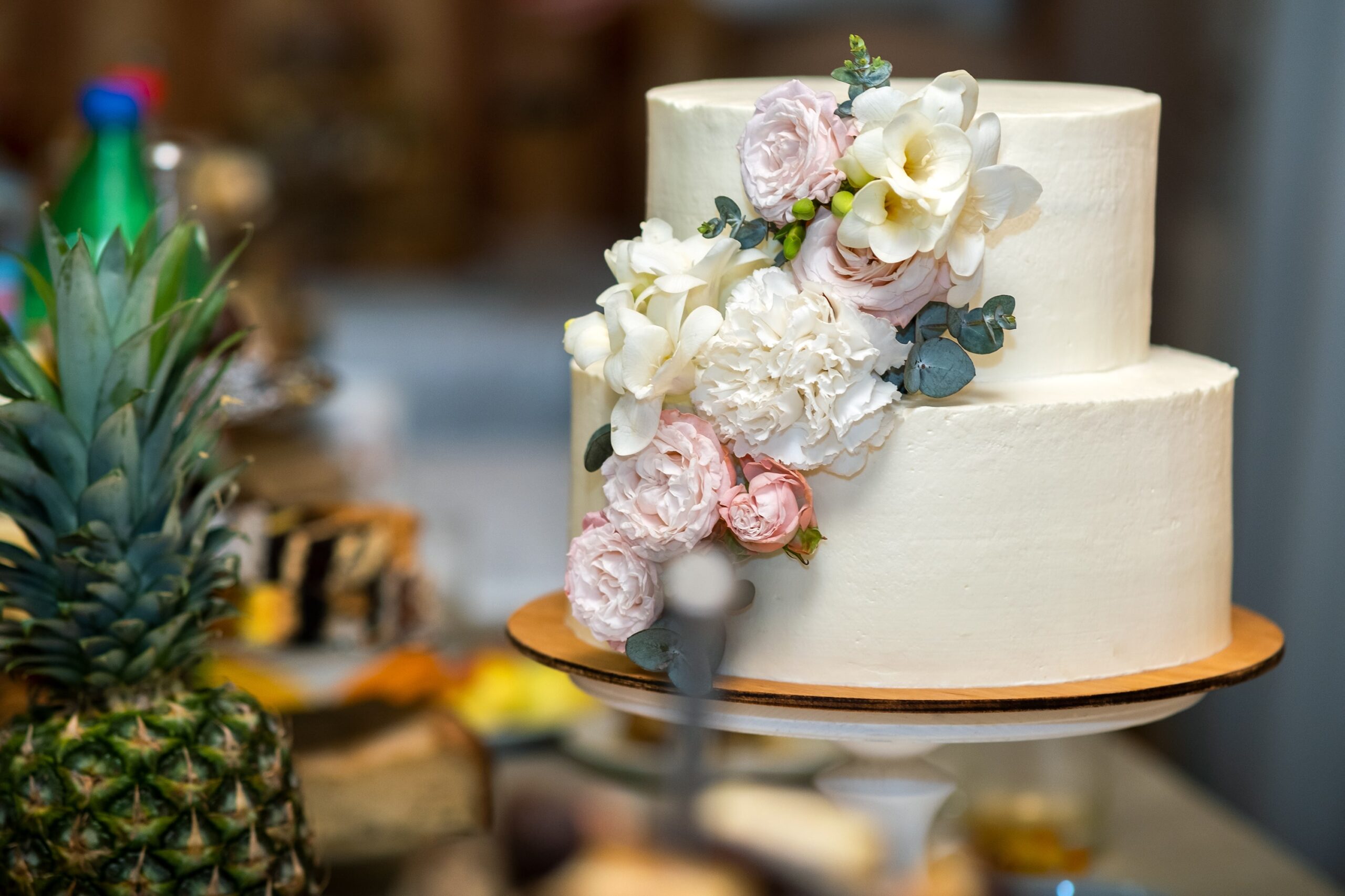 A two-tiered wedding cake adorned with fresh pink and white flowers cascading down the side.