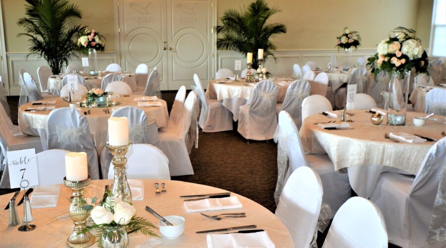 Elegantly decorated reception venue with round tables draped in white linens, floral centerpieces, and candles, creating a sophisticated and inviting atmosphere.