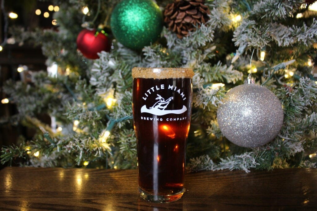 A  glass of Little Miami Brewing Company's flavored beer with a festive holiday rim, set against a decorated Christmas tree.