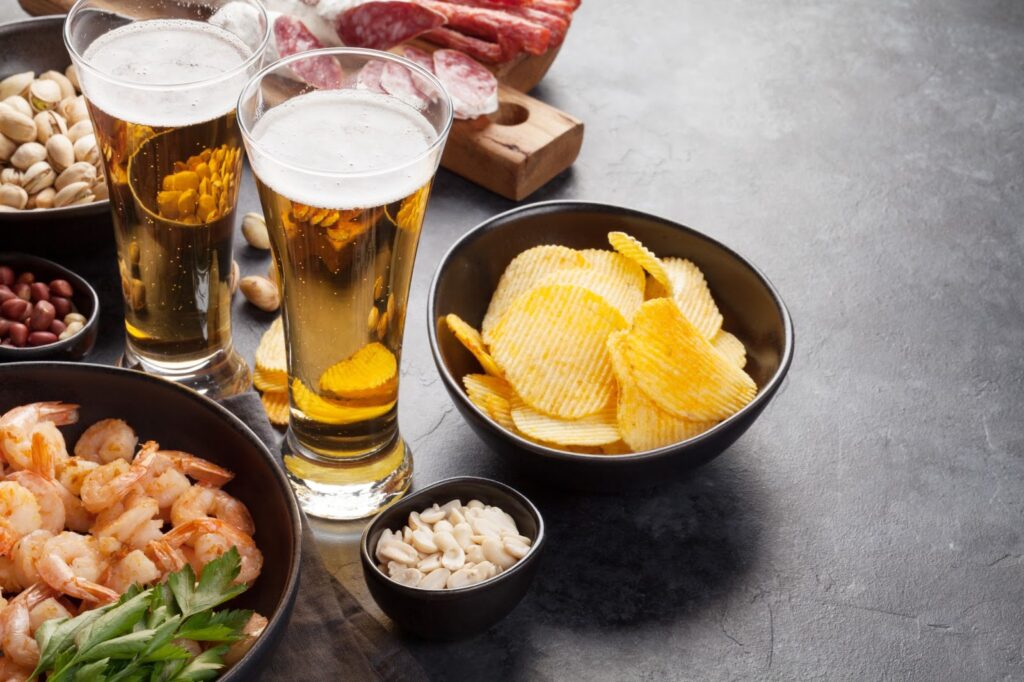 Two glasses of IPAs paired with shrimp, chips, nuts, and charcuterie for a delicious food and beer combination.