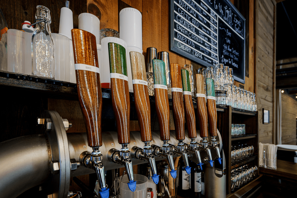 A close-up of a bar with several beer taps, each with a different colored handle and a variety of beer glasses lined up on the shelf.