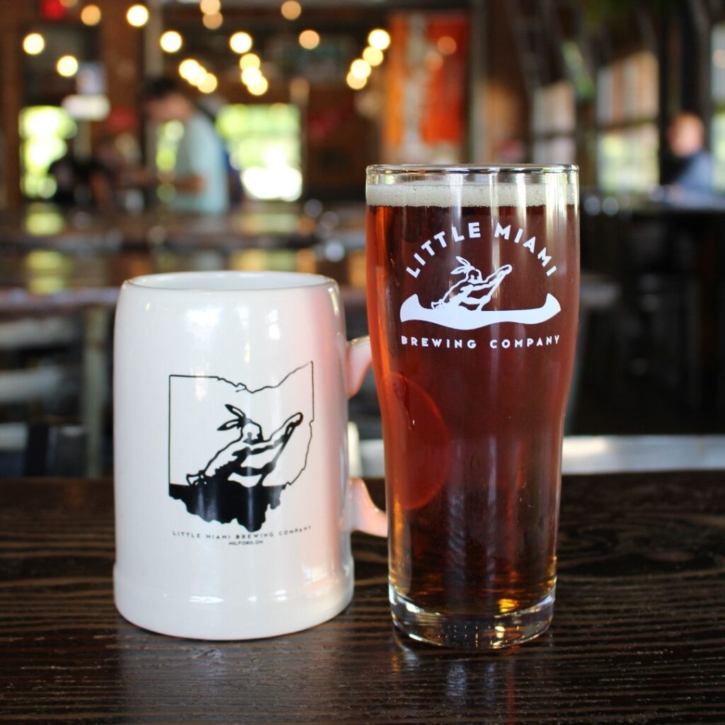 Little Miami Beer and a ceramic mug on a dark wooden table.