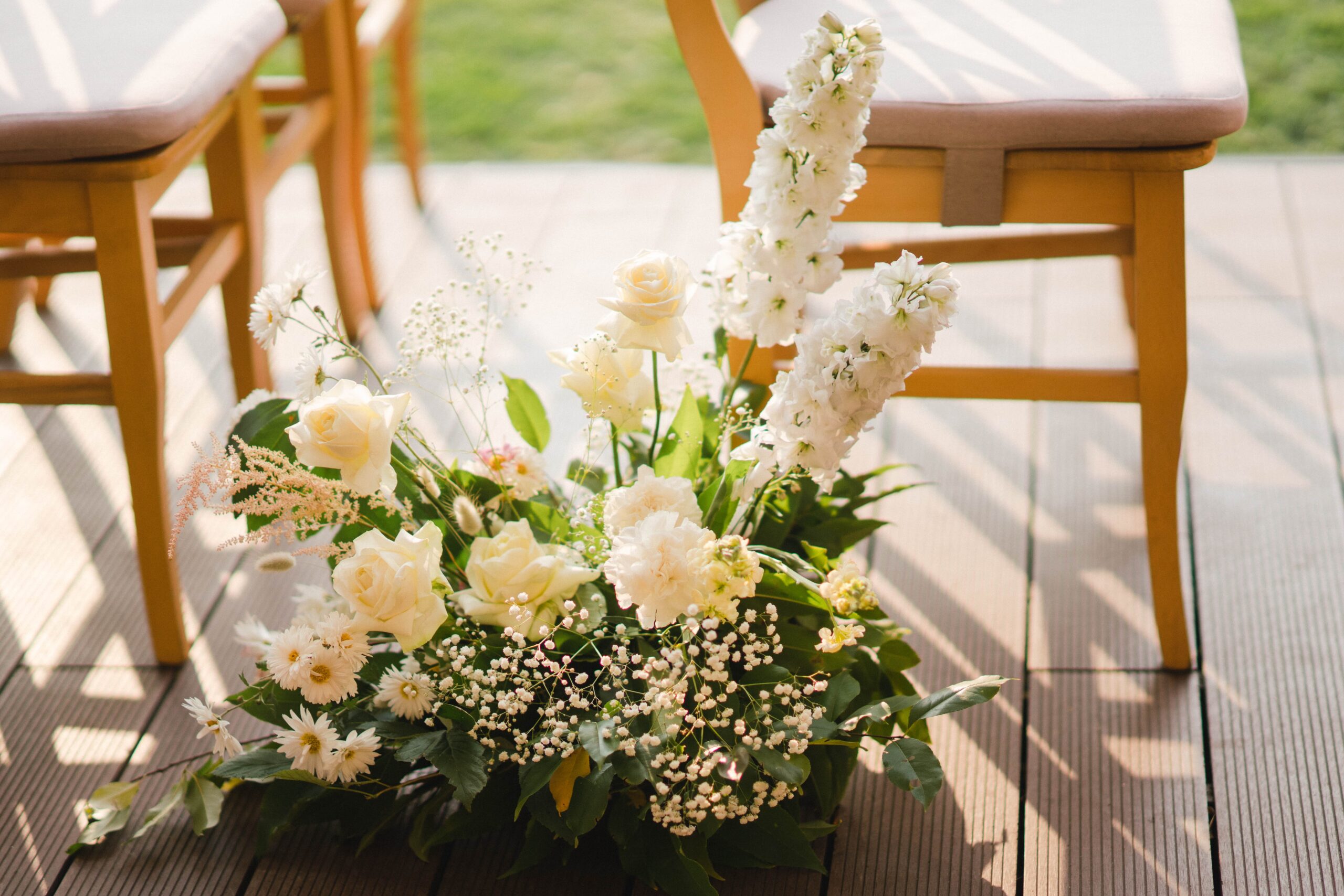 A delicate floral arrangements featuring white roses, baby's breath, and greenery, perfect for wedding aisle decor.