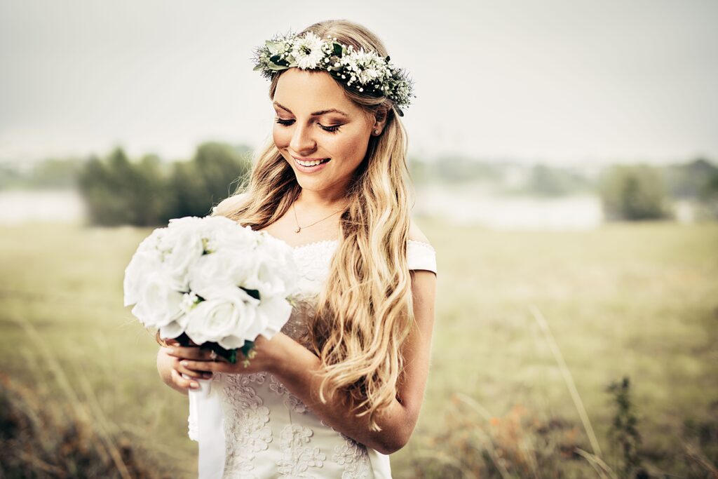 Bride embracing a floral rustic wedding theme, holding a white bouquet and wearing a flower crown in an outdoor countryside setting.