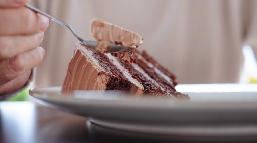 A close-up shot of a hand scooping a bite of rich, chocolate cake with a silver spoon.