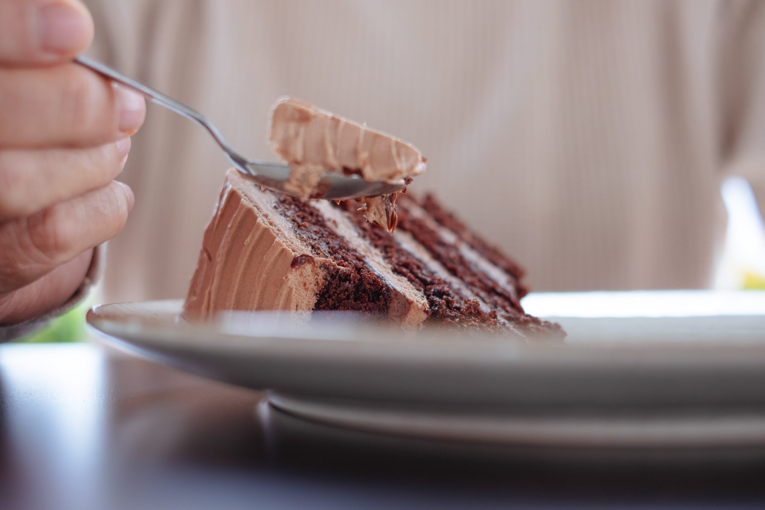 A close-up shot of a hand scooping a bite of rich, chocolate cake with a silver spoon.