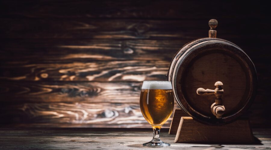 Shot of a barrel-aged glass of beer next to the barrel it was aged in.