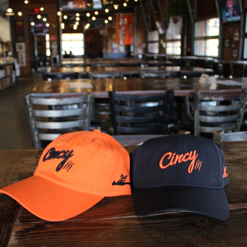 Two ‘Cincy’ baseball caps, one orange and one black, from Little Miami Brewing Company.