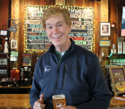 A light-skinned man stands in a brewery, holding a glass of Little Miami Brewing Company beer and giving a thumbs up.