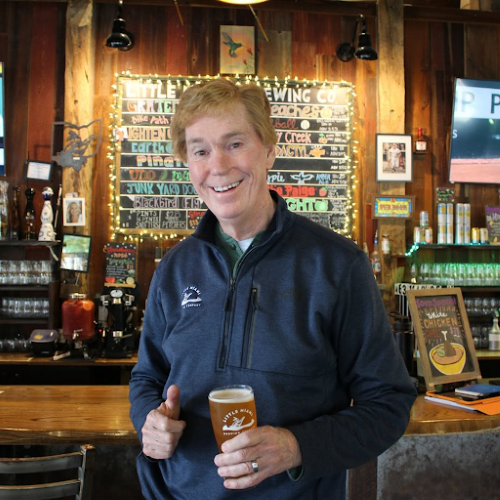 A light-skinned man stands in a brewery, holding a glass of Little Miami Brewing Company beer and giving a thumbs up.