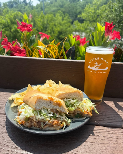 A vibrant outdoor scene features a sandwich with chips and a beer from Little Miami Brewing Company.