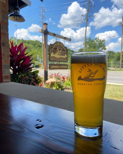 A glass of Little Miami Brewing beer on a table with the brewery's wooden sign in the background during sunset.