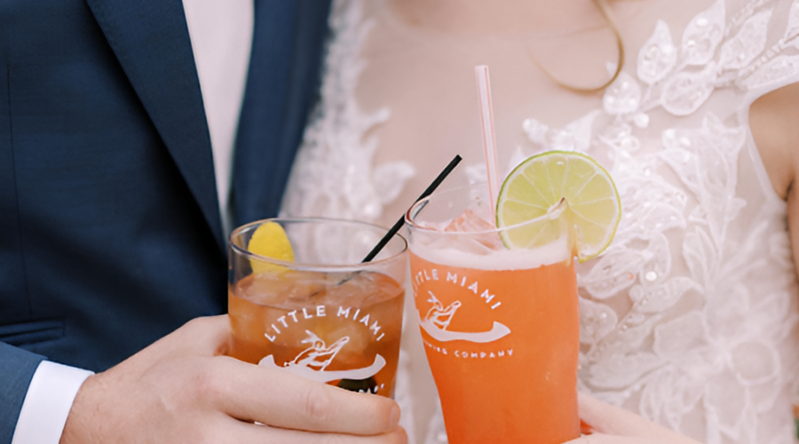 A couple in wedding attire toasts with "Little Miami Brewing Company" drinks at their wedding.