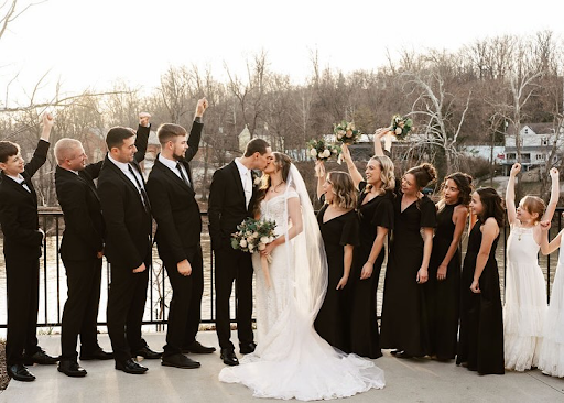 Bride and groom kiss while surrounded by their wedding party beside the Little Miami River at sunset in Cincinnati.