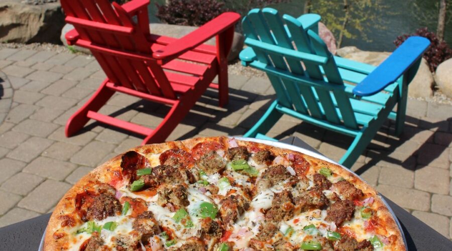 Brick-oven pizza from Little Miami Brewing Company served on a riverside table with red and blue chairs overlooking the Little Miami River.