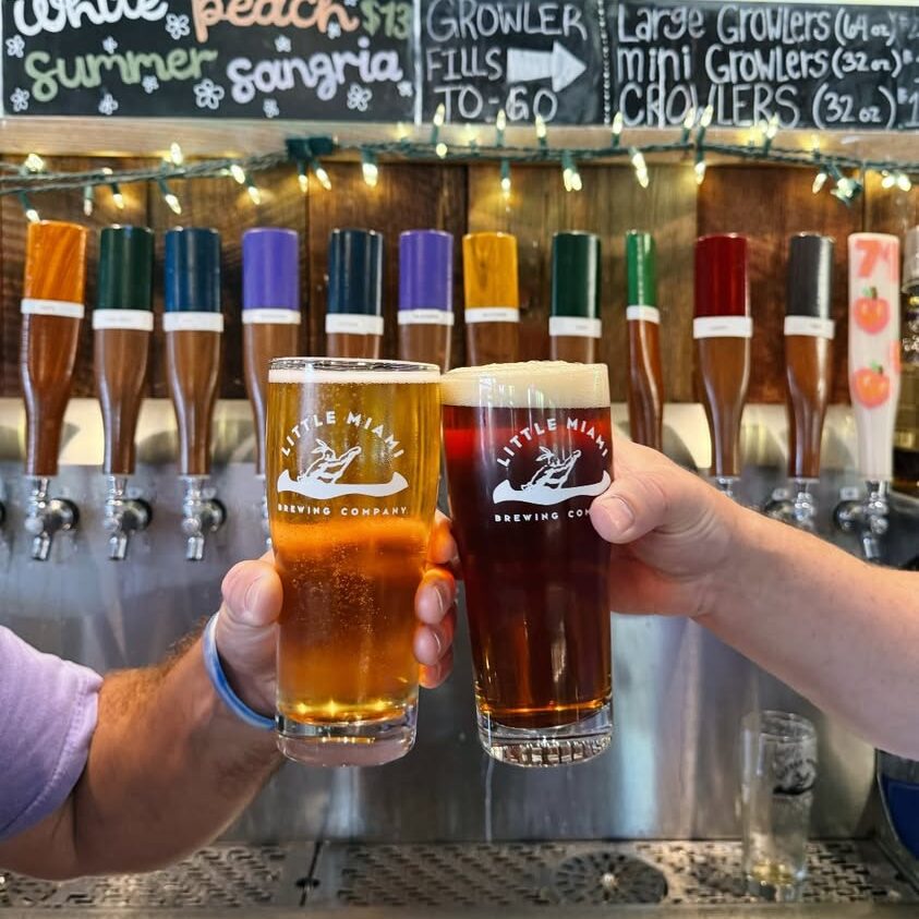 Two people clinking different beers at Little Miami Brewing Company.