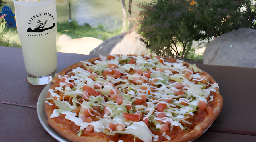 A loaded pizza and a pint from Little Miami Brewing Company on a wooden table in front of a lush riverside.