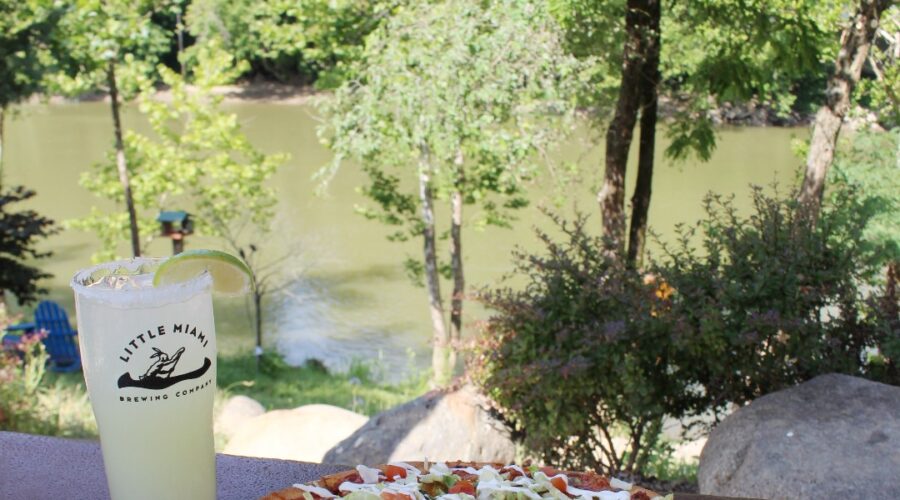 A pizza and margarita cocktail on a rustic wooden table overlooking the Little Miami River at Little Miami Brewing Company.