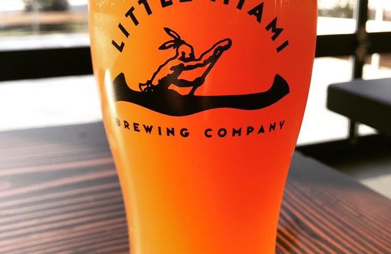 Cascade Hazy IPA by Little Miami Brewing Company served in a pint glass on a wooden table.