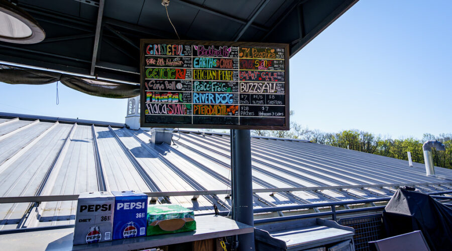 LMBC’s outdoor beer menu board listing brews, with Pepsi boxes and bar gear stacked below.