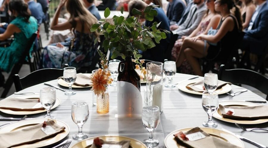 An elegant outdoor reception table setting at Little Miami Brewing Co., with wedding guests seated in the background.